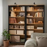 Étagère en bois avec garniture sombre, livres et décoration, lampes au-dessus, fauteuil.