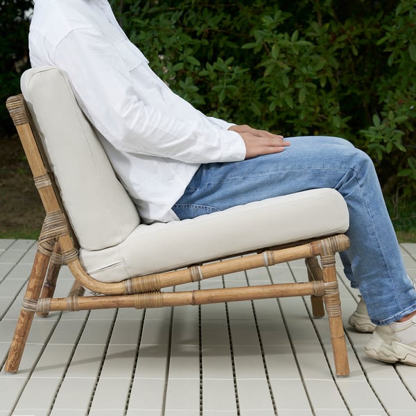 Personne assise sur une chaise en osier avec un coussin sur un patio carrelé.