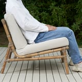 Personne assise sur une chaise en osier avec un coussin sur un patio carrelé.