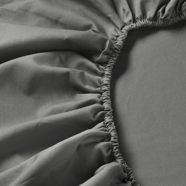 Gros plan du drap-housse avec bords élastiques. Tissu doux et densément tissé, affichant des coutures fines et une texture lisse.