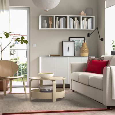 Salon avec tapis gris, table basse, canapé, étagère, chaise, lampe, plantes, porte de jardin.