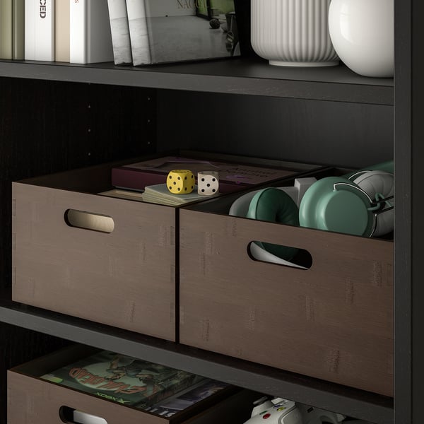 Étagère avec des boîtes en bambou teinté foncé, des objets de rangement, des accessoires de jeu et un vase décoratif.