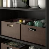 Étagère avec des boîtes en bambou teinté foncé, des objets de rangement, des accessoires de jeu et un vase décoratif.