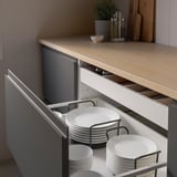 Tiroir de cuisine avec organisateur ouvert montrant des assiettes blanches empilées maintenues par des supports métalliques.