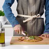 Personne en tablier coupant une pizza avec un emporte-pièce ikea sur une planche de bois.