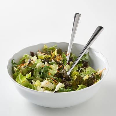 Bol en porcelaine blanche à bord ébouriffé, rempli de salade. Deux cuillères de service en sortent. Léger, durable, lavable au lave-vaisselle.