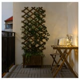 Balcon confortable avec table en bois, chaise, lumières UTSUND et treillis de plantes.