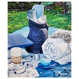 L’image montre une lanterne extérieure bleue UTSUND avec une nappe florale, des assiettes et un sac à dos sur une couverture.