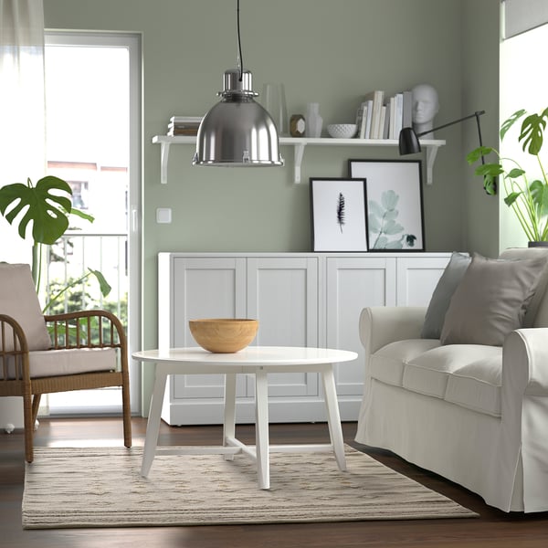 Salon confortable avec murs verts, chaise blanche, table ronde et grand tapis traditionnel.