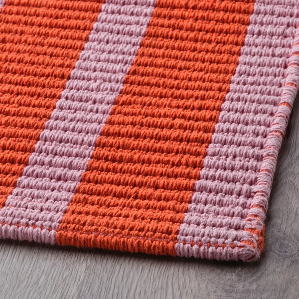 Tapis en coton rayé rose vif et orange, soigneusement plié. Surface texturée et tissée, couleurs vives.