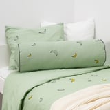 Lit avec des oreillers banane verts, un coussin de soutien dorsal rectangulaire contre le mur, des draps crème vif et une tête de lit blanche.
