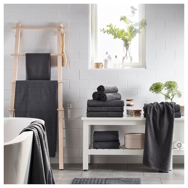 Salle de bain moderne avec serviettes VÅGSJÖN gris foncé et peignoir sur une échelle en bois, unité de rangement blanche et plantes.