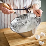 La personne fouette le mélange dans un grand bol en acier inoxydable. Le bol a un bec verseur pour un versement facile.