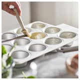 Personne graissant le moule à muffins VARDAGEN, argenté, avec un pinceau, se préparant à cuire.