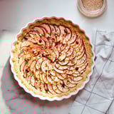 Plat à tarte blanc à bords ondulés avec tarte aux pommes, sur marbre, tissu rayé.