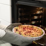 Personne tenant une tarte cuite dans un plat près du four. Les gants de cuisine protègent les mains.