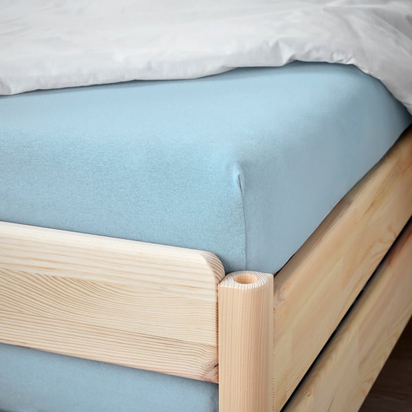 Un drap bleu clair sur un cadre de lit en bois.