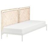 Un lit VEVELSTAD avec un cadre en métal blanc et une tête de lit en rotin naturel, combinant des éléments modernes et naturels.