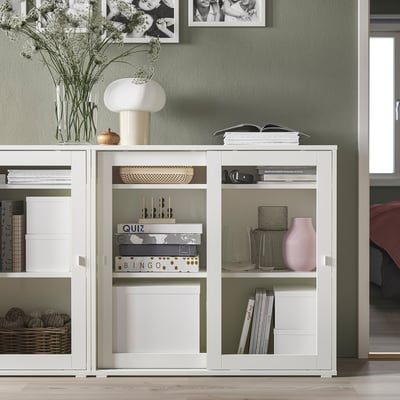 Armoire moderne à portes vitrées blanches, plus petite que les meubles environnants, décorée avec des vases, des livres et de la décoration.