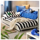 Chambre confortable avec lit de repos à rayures blanches et noires, draps bleus et animaux en peluche.