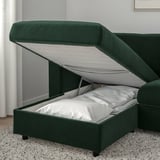 Canapé vert foncé avec un compartiment de rangement surélevé et accessible sous le siège, montrant les oreillers à l’intérieur.