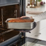 Une personne utilisant un moule à pain pour cuire du pain dans un four. Le moule assure une répartition uniforme de la chaleur pour une cuisson dorée.