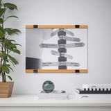 Porte-affiches mural à deux parties tenant une affiche de signalisation directionnelle, soutenu par une étagère en bois avec une plante et des objets décoratifs.