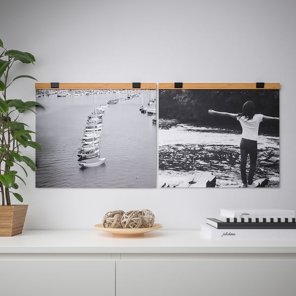 Deux affiches de port de plaisance en noir et blanc sont accrochées sur un mur gris clair à l’aide d’un cintre VISBÄCK en bois. En dessous, une étagère blanche contient des plantes, des cordes et des livres.