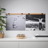 Deux affiches de port de plaisance en noir et blanc sont accrochées sur un mur gris clair à l’aide d’un cintre VISBÄCK en bois. En dessous, une étagère blanche contient des plantes, des cordes et des livres.