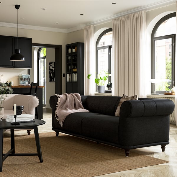 Salon moderne avec canapé noir, formes arrondies, table basse, fenêtres cintrées, atmosphère chaleureuse.