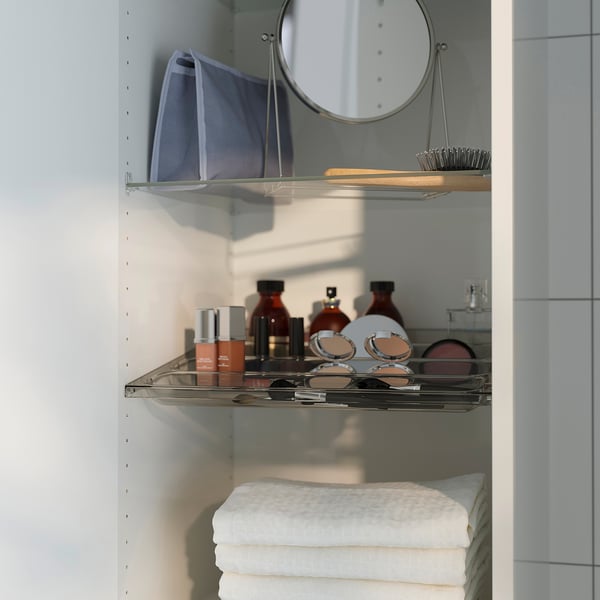 Étagère ouverte avec cosmétiques et serviettes. Montre un miroir rond, des articles de maquillage et un sac bleu.