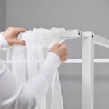 Personne ajustant des rideaux transparents blancs sur un cadre de lits à baldaquin VITARNA.