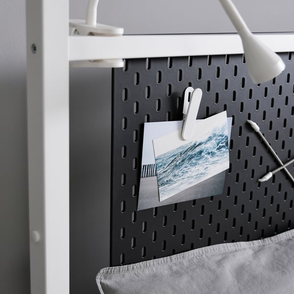 Panneau perforé noir avec des clips blancs tenant un paysage marin. Une lampe de bureau est fixée dans le coin supérieur droit du tableau.