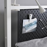 Panneau perforé noir avec des clips blancs tenant un paysage marin. Une lampe de bureau est fixée dans le coin supérieur droit du tableau.