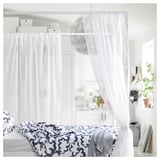 Lit avec rideaux blancs, couverture à motifs bleus et oreillers blancs.