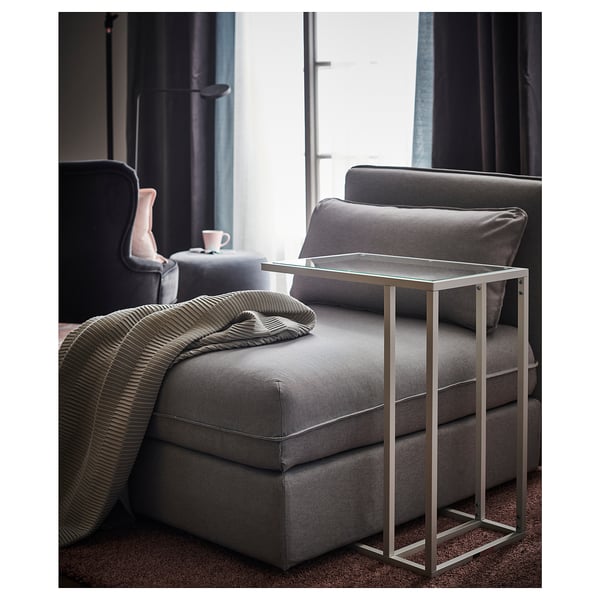 Salon moderne avec fauteuil inclinable en tissu gris, petite table avec plateau en verre et couverture rayée.