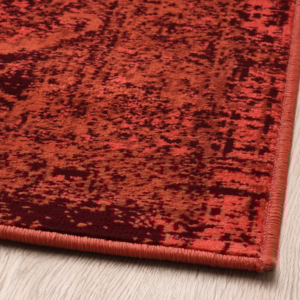 Tapis à motifs rouges vifs, doux au toucher, avec un look vintage usé, posé sur un plancher en bois.
