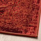 Tapis à motifs rouges vifs, doux au toucher, avec un look vintage usé, posé sur un plancher en bois.