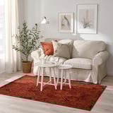 Salon confortable avec canapé VONSBÄK beige, coussins orange/blanc, tapis rouge, table, plante, décoration chaleureuse.