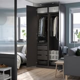 Chambre moderne avec armoire ouverte, avec cintres, tiroirs et une lampe LED YTBERG noire fixée sur le dessus, fournissant un éclairage réglable.