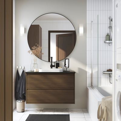 Moderne badkamer met ÄNGSJÖN notenhouten kast, wit aanrechtblad en wastafel; Grote ronde spiegel, aan de muur bevestigd voor een ruimtelijk gevoel.