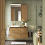 Moderne badkamer met groene tegels, eikenhouten kast, witte wastafel, grote spiegel en glazen douche. Minimalistisch ontwerp.