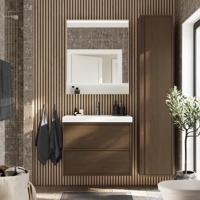 Moderne badkamer met ÄNGSJÖN bruine notenhouten kast, grote spiegel, witte wastafel, grijze handdoeken en groene plant.