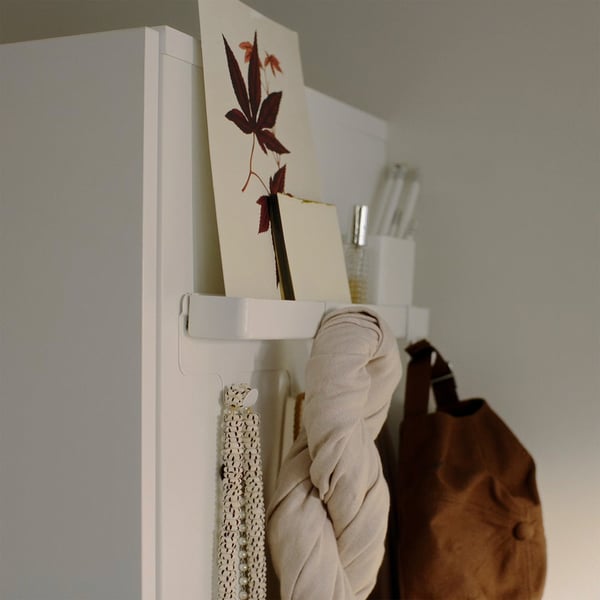 Witte wandrek met hangende items: stof, ketting en kunstwerken.