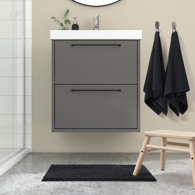 Moderne badkamer met BACKMÅRA grijze mat, hangende handdoeken, grijze badmeubel en houten kruk. Mat is zacht en past goed onder de ijdelheid.