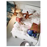 Het kind speelt op bed met hart-patroon wit dekbed, bruine teddybeer, en blauw kattenspeeltje.