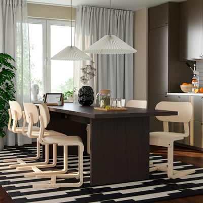 Moderne eetkamer met donkere tafel, houten stoelen, gestreept tapijt, plant, lampen en grijze gordijnen.