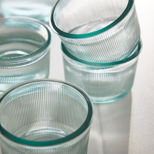 Vier groen getinte glazen met geribbelde motieven zitten op een wit oppervlak en tonen hun textuur van gerecycled glas en de aangenaam in de hand liggende, brede vorm.