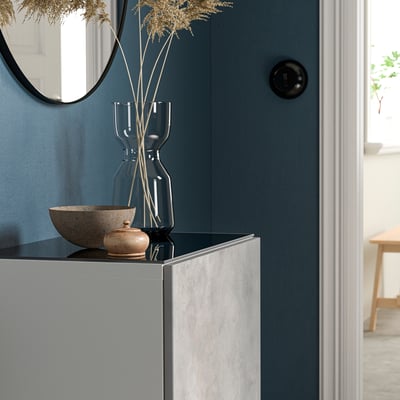 Een BESTÅ glazen bovenpaneel in blauw, rechthoekig, met een modern design, is groot en staat bovenop een kast, met decoratieve voorwerpen.