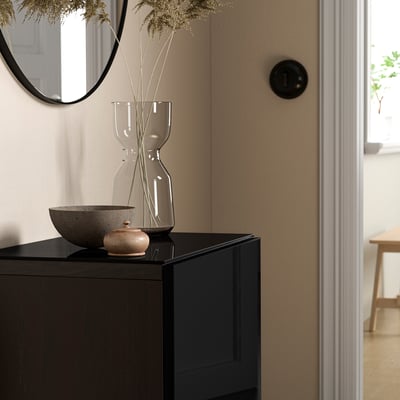 Moderne woonkamer met BESTÅ opbergkast, zwart glazen blad, minimalistische inrichting en gedroogde bloemen in een vaas.